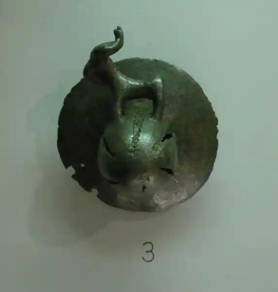 A circular bronze buckle engraved with a cross and an animal on top